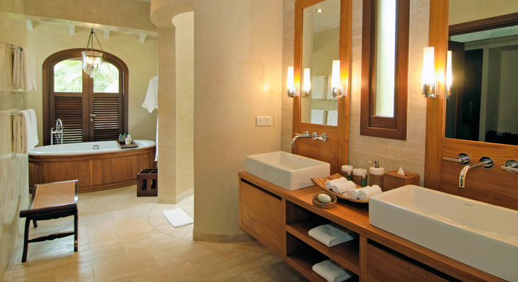 Spacious spa bathroom with double vessel sinks, wooden vanity, and a soaking tub in a soft warm alcove
