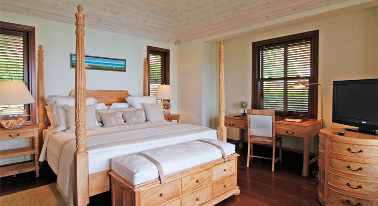 Hotel bedroom with a wooden four-poster bed, white linens, dark wood shuttered windows, warm cozy mood